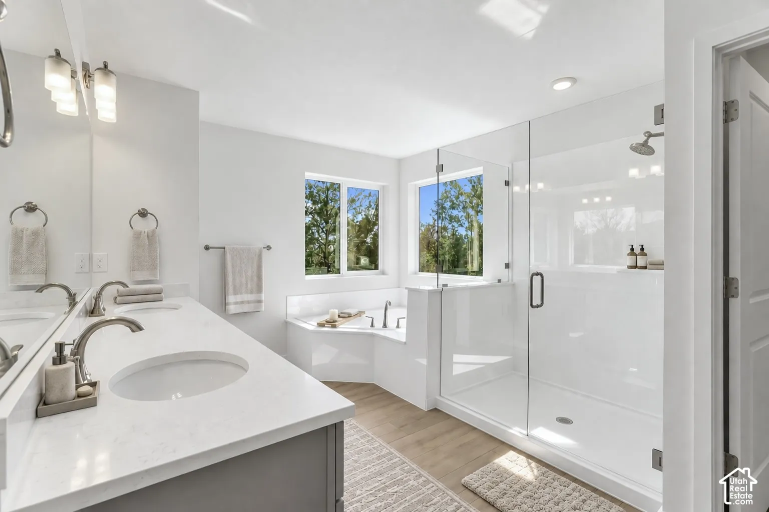 Dual vanity with undermount sinks and extensive countertop space, glass-enclosed shower, built-in soaking tub, and light wood-finish flooring