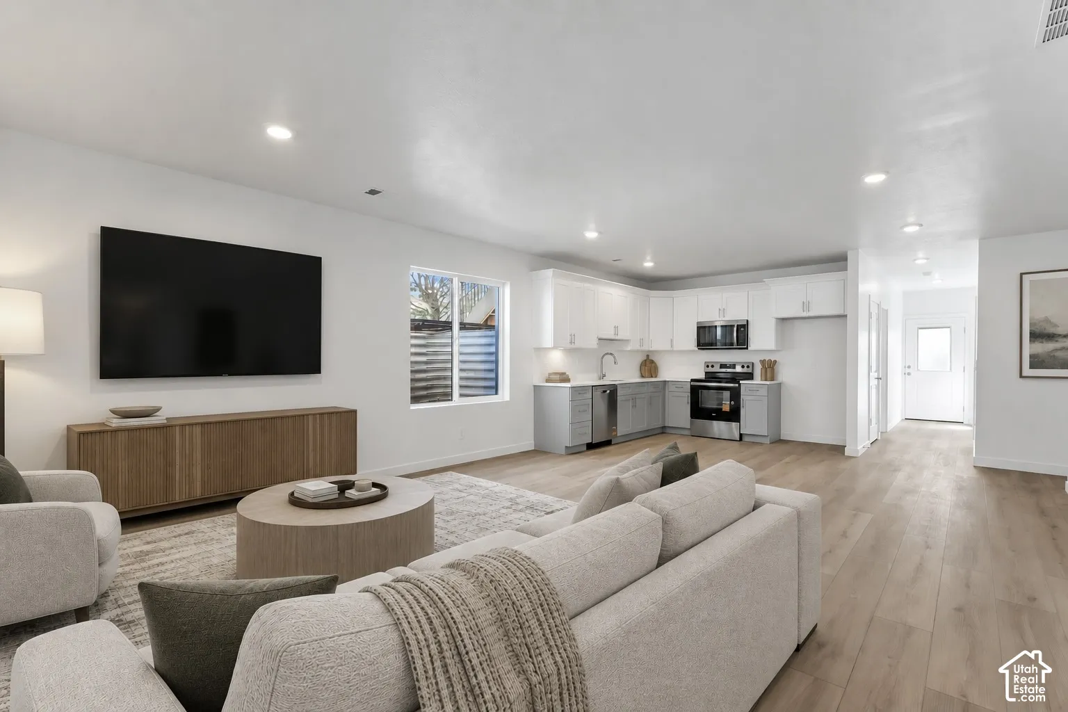 Open-concept living space featuring wood-finish flooring, recessed lighting, and a modern kitchen with two-tone cabinetry and stainless-steel appliances