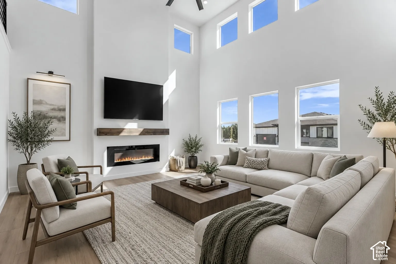 Soaring ceilings with upper transom windows, linear electric fireplace with wood-finish mantel, and wood-finish flooring