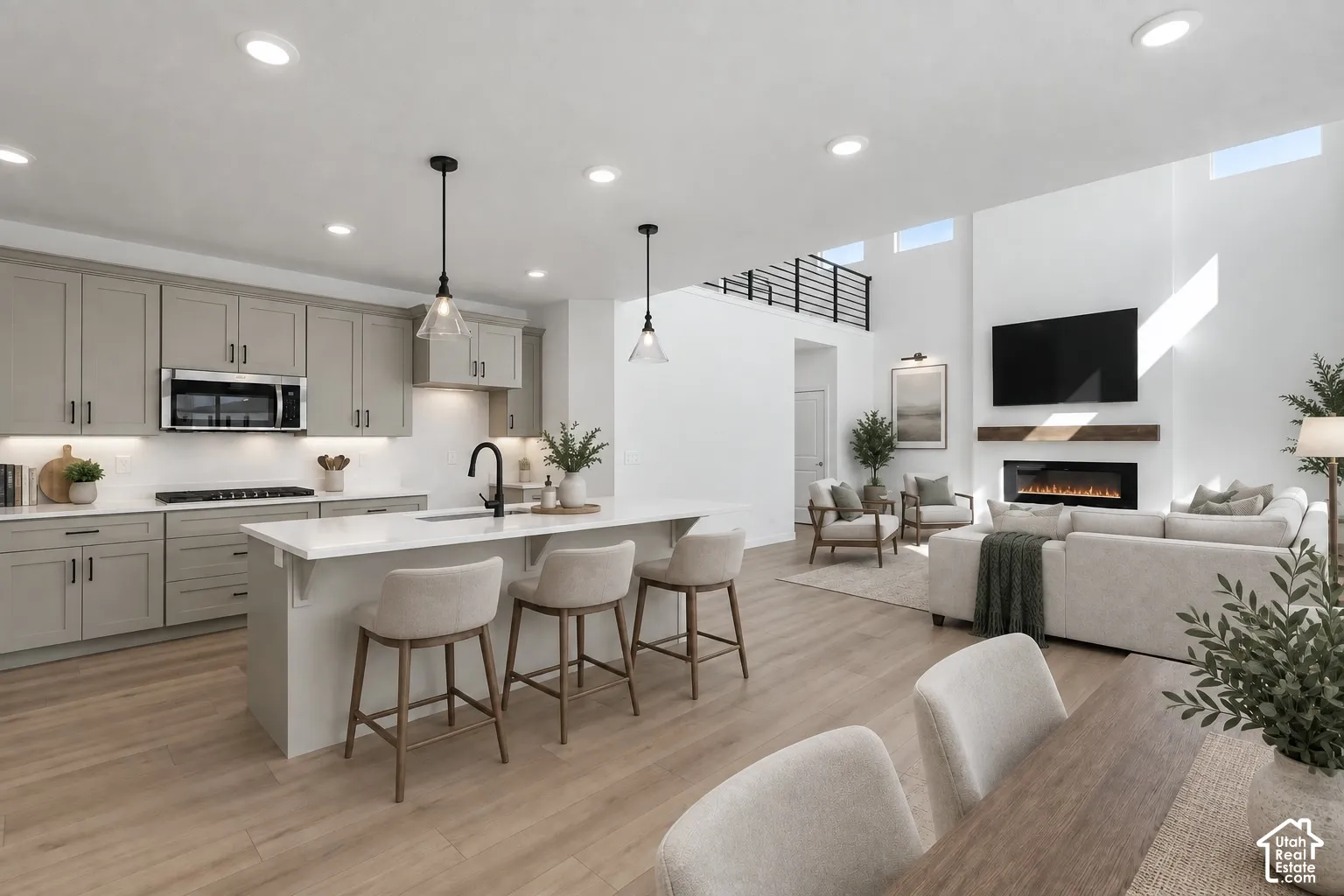 Open-concept living space with wood-finish flooring, a kitchen island with seating, a built-in fireplace, and high ceilings with upper windows