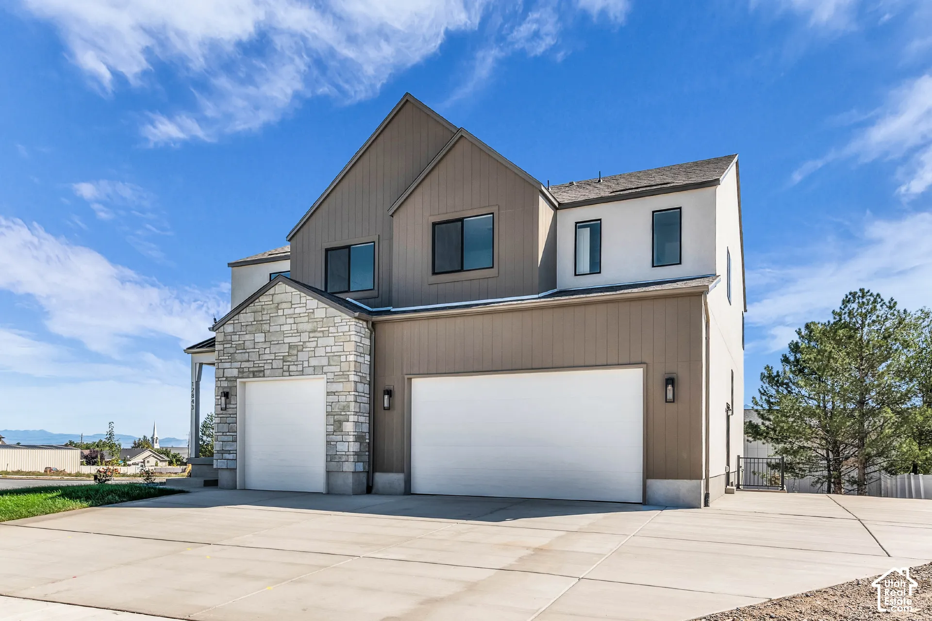 Multi-level exterior featuring mixed material facade, stone accents, two garage doors, and dark window frames