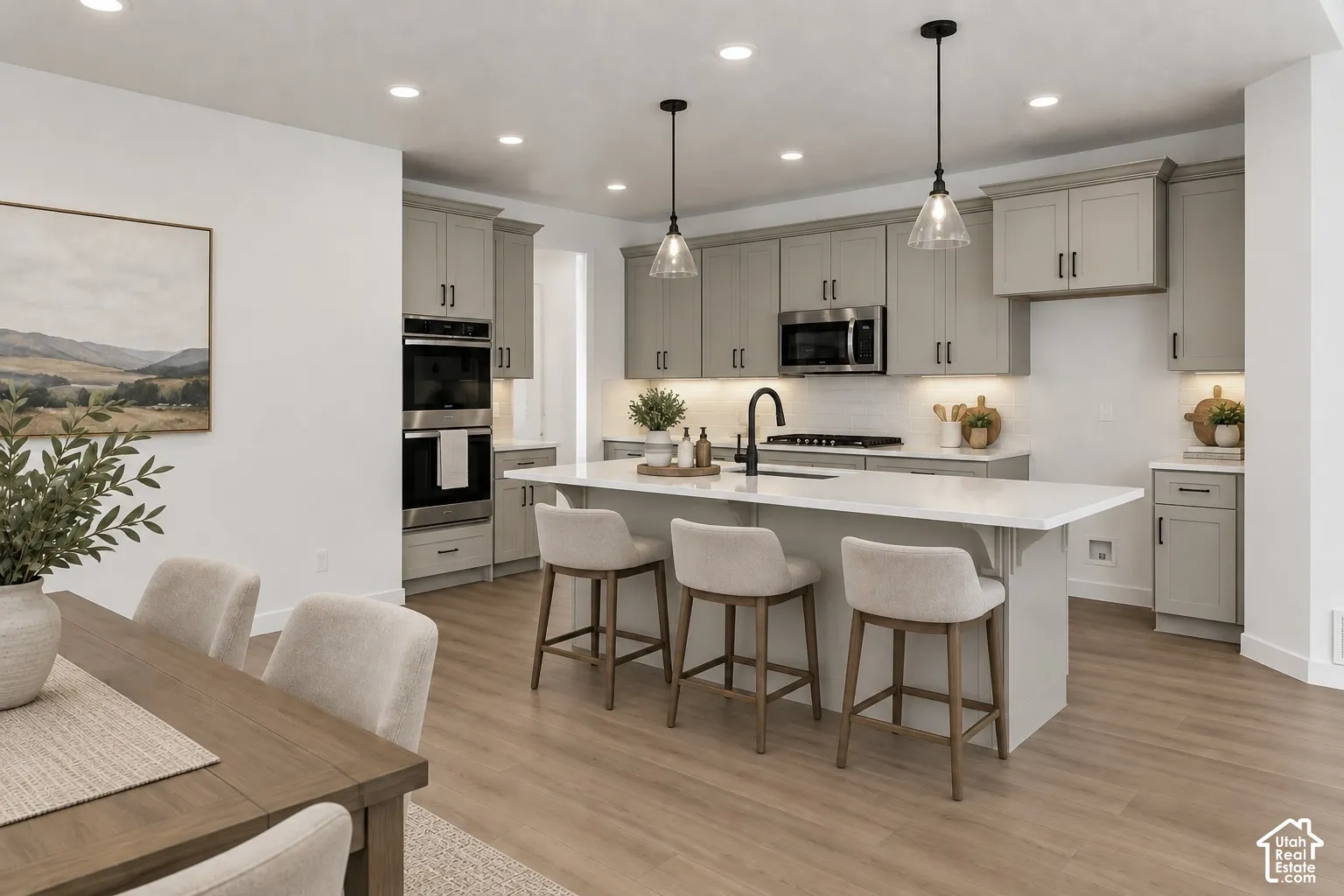 Modern kitchen featuring light wood-finish flooring, light gray cabinetry with black hardware, white countertops, built-in stainless steel appliances, and an expansive center island with pendant lighting