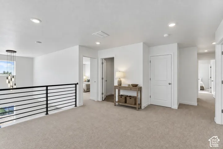 Spacious carpeted loft with recessed lighting, modern linear chandelier, and contemporary black metal railing