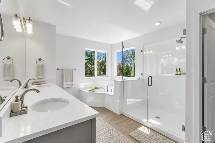 Dual vanity with undermount sinks and extensive countertop space, glass-enclosed shower, built-in soaking tub, and light wood-finish flooring