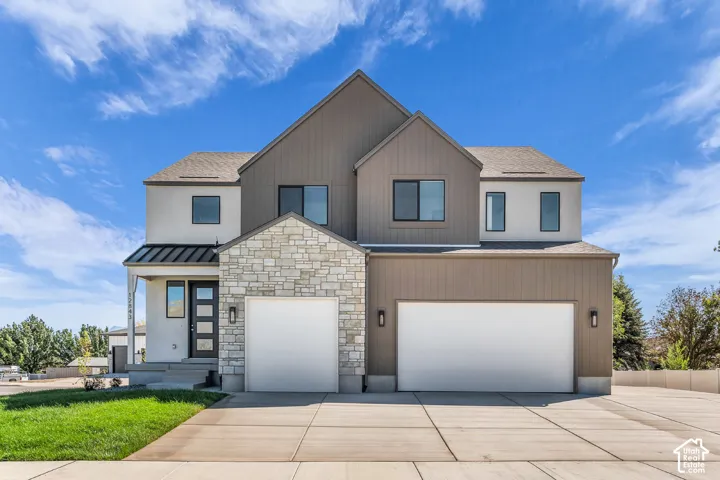 Modern exterior featuring mixed materials, two-car garage, prominent stone accents, board-and-batten siding, and a covered entry