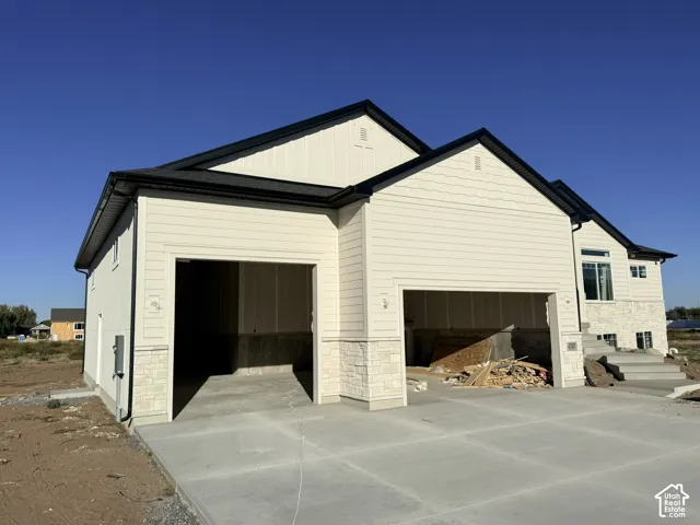 Two-car garage with concrete driveway, light-toned siding, and stone accents