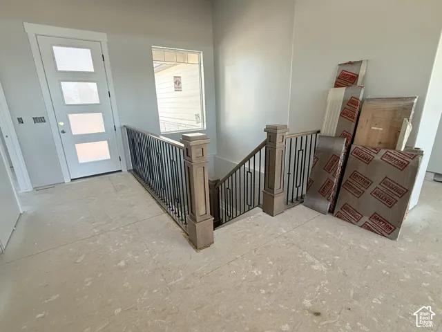 Entryway featuring a four-panel glass-inset door, natural light from a square window, and a staircase with wood newel posts and metal balusters