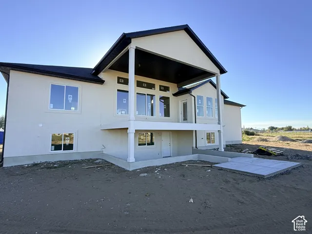 Rear exterior featuring a covered deck with white columns, stucco siding, and a concrete patio slab
