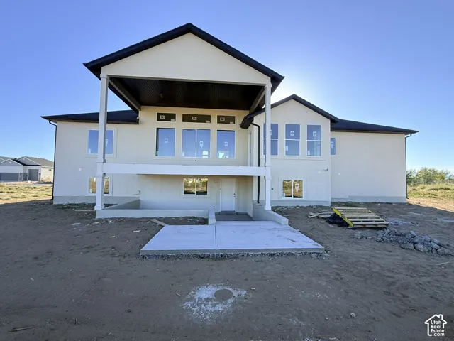 Stucco exterior with multiple windows, covered upper-level deck, lower-level concrete patio, and dark shingle roofing