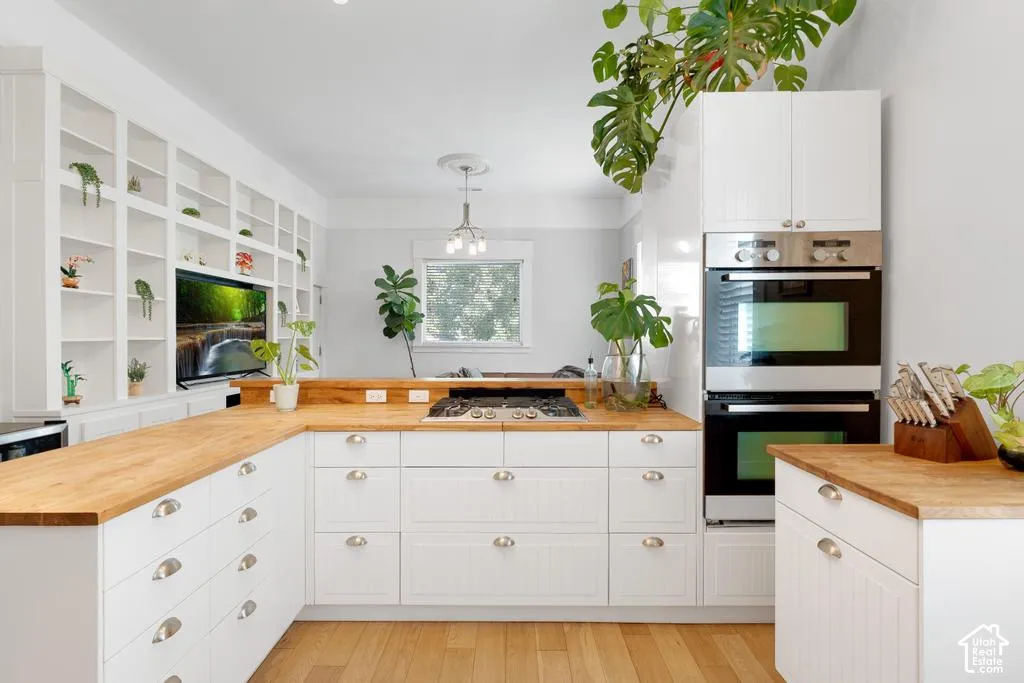 White cabinetry with cup pull hardware, natural wood-finish countertops, built-in wall ovens, and integrated shelving