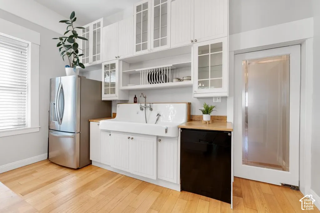 White cabinetry with glass-front uppers, stainless steel refrigerator, white farmhouse-style sink, wood-finish countertops, and wood-finish flooring