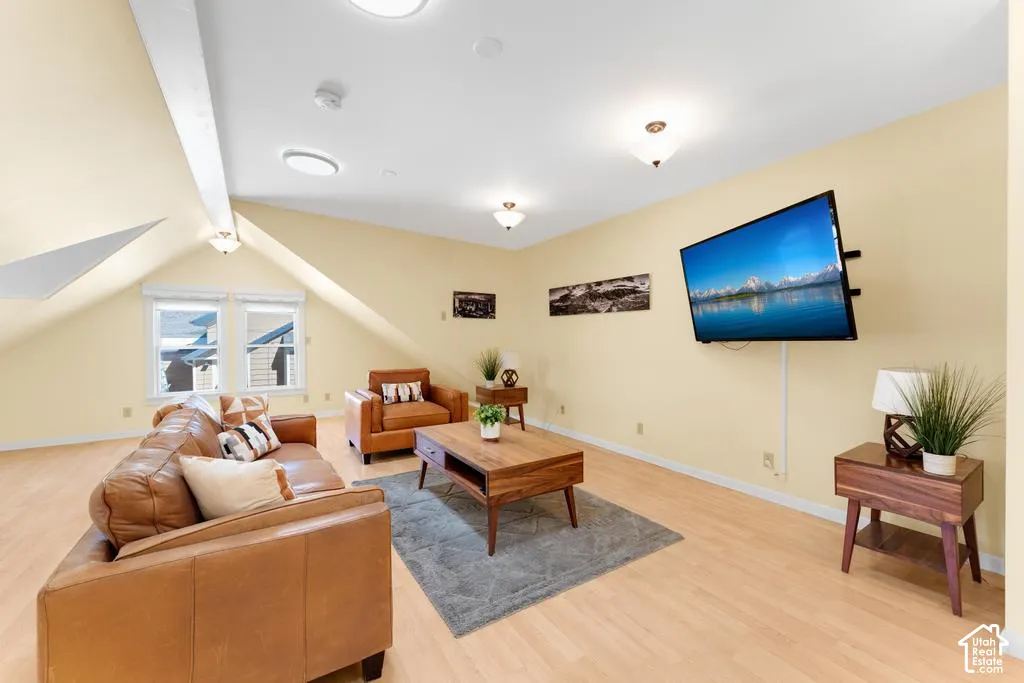 Sloped ceiling with recessed and flush-mount lighting, light wood-finish flooring, and multiple windows