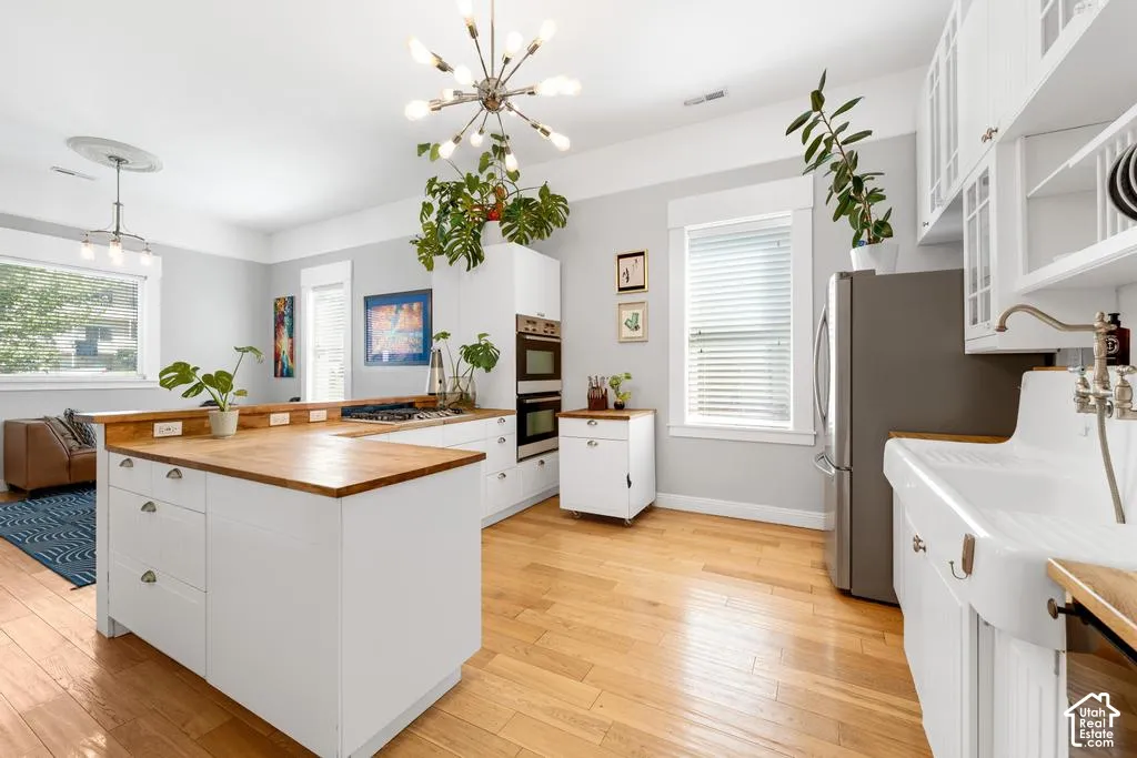 Open-concept kitchen with wood-finish flooring, white cabinetry, integrated double ovens, and a large farmhouse sink
