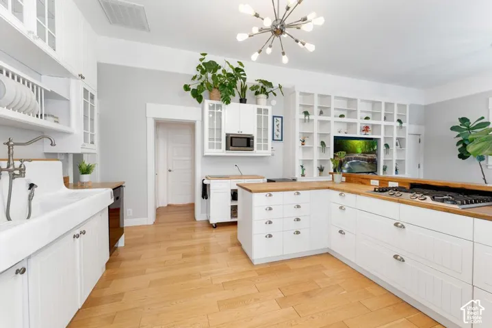 Spacious kitchen featuring light wood-finish flooring, white cabinetry, wood countertops, and a built-in wall unit