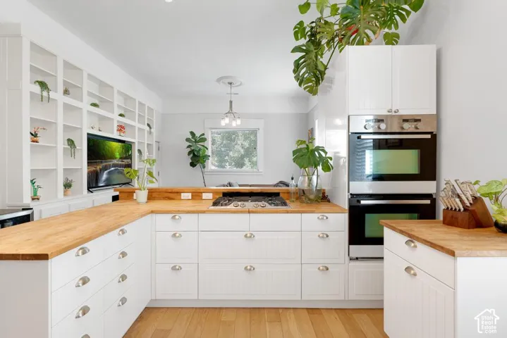 White cabinetry with cup pull hardware, natural wood-finish countertops, built-in wall ovens, and integrated shelving