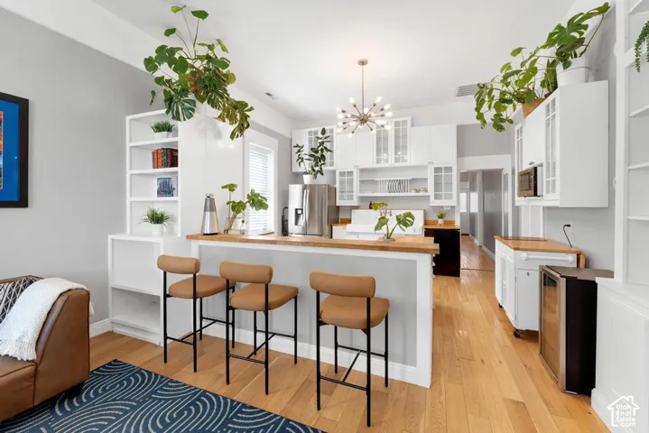 Hardwood-finish flooring, white built-in shelving, white cabinetry with glass inserts, light wood-finish countertops, and a modern sputnik chandelier