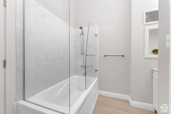 Bathtub with jets, glass shower enclosure, full wall tile surround, shower wand, and wood-finish flooring