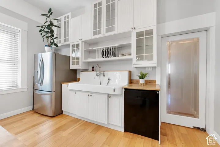 White cabinetry with glass-front uppers, stainless steel refrigerator, white farmhouse-style sink, wood-finish countertops, and wood-finish flooring