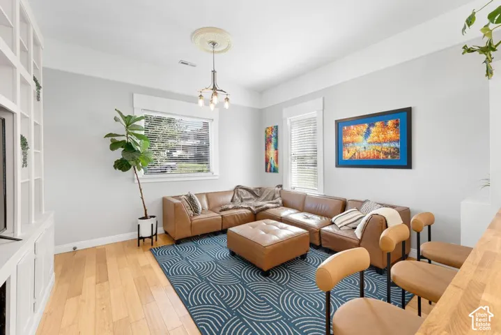 Light wood-finish flooring, built-in shelving, windows with blinds, and a decorative ceiling medallion with a chandelier