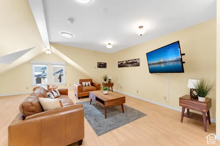 Sloped ceiling with recessed and flush-mount lighting, light wood-finish flooring, and multiple windows