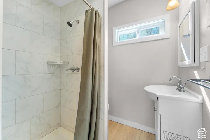 Tiled shower surround with a showerhead and separate controls, a pedestal-style sink with a chrome faucet, and a horizontally oriented window