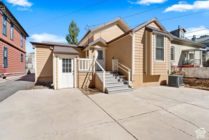 Concrete patio with a staircase leading to a rear entrance, featuring an exterior door with glass panes, and an additional exterior door on a smaller structure