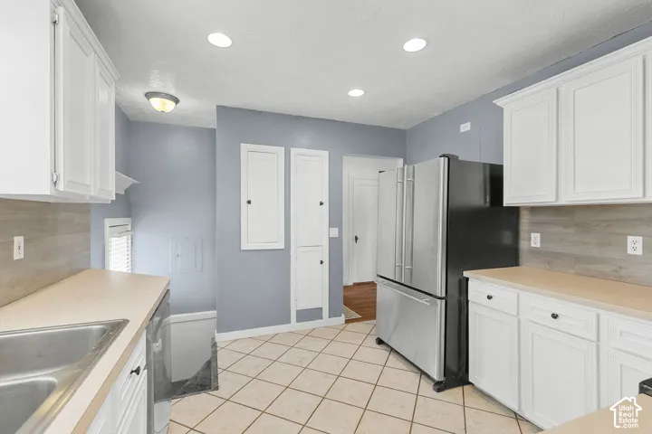White cabinetry with dark hardware, a stainless steel refrigerator, tile flooring, and a light-toned countertop