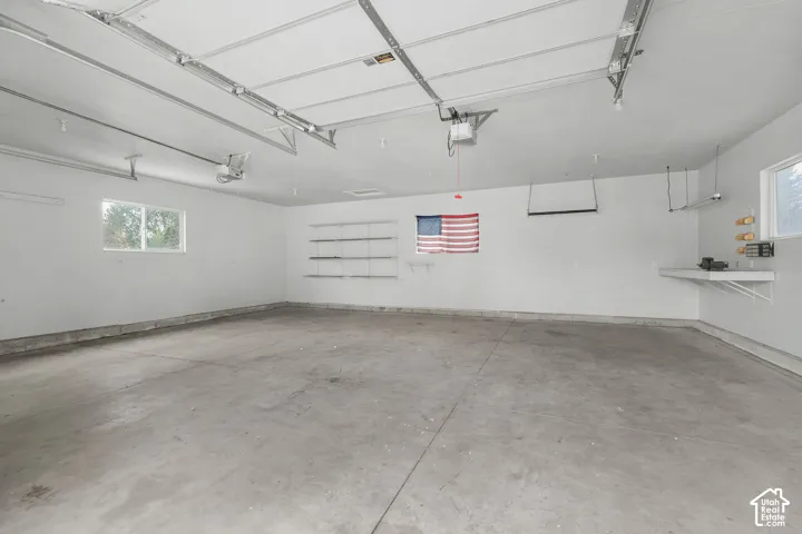 Expansive garage with durable concrete flooring, multiple windows, built-in shelving, and a workbench