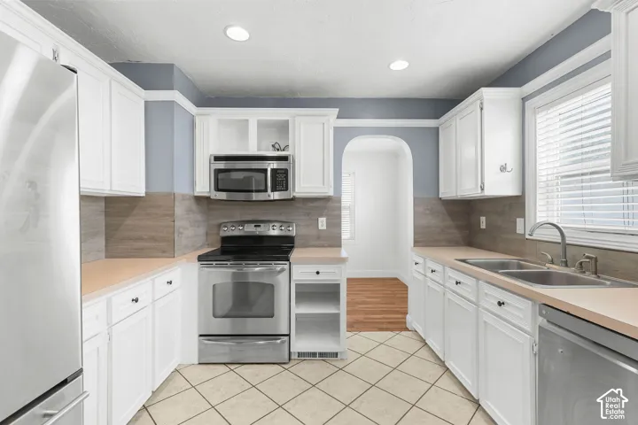 White cabinetry with dark hardware, stainless steel appliances, dual basin sink, light-toned countertops, and tile flooring