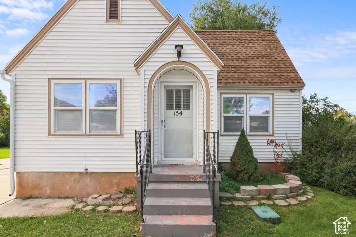 White siding exterior with a shingled roof, arched entry frame, and black wrought iron handrails