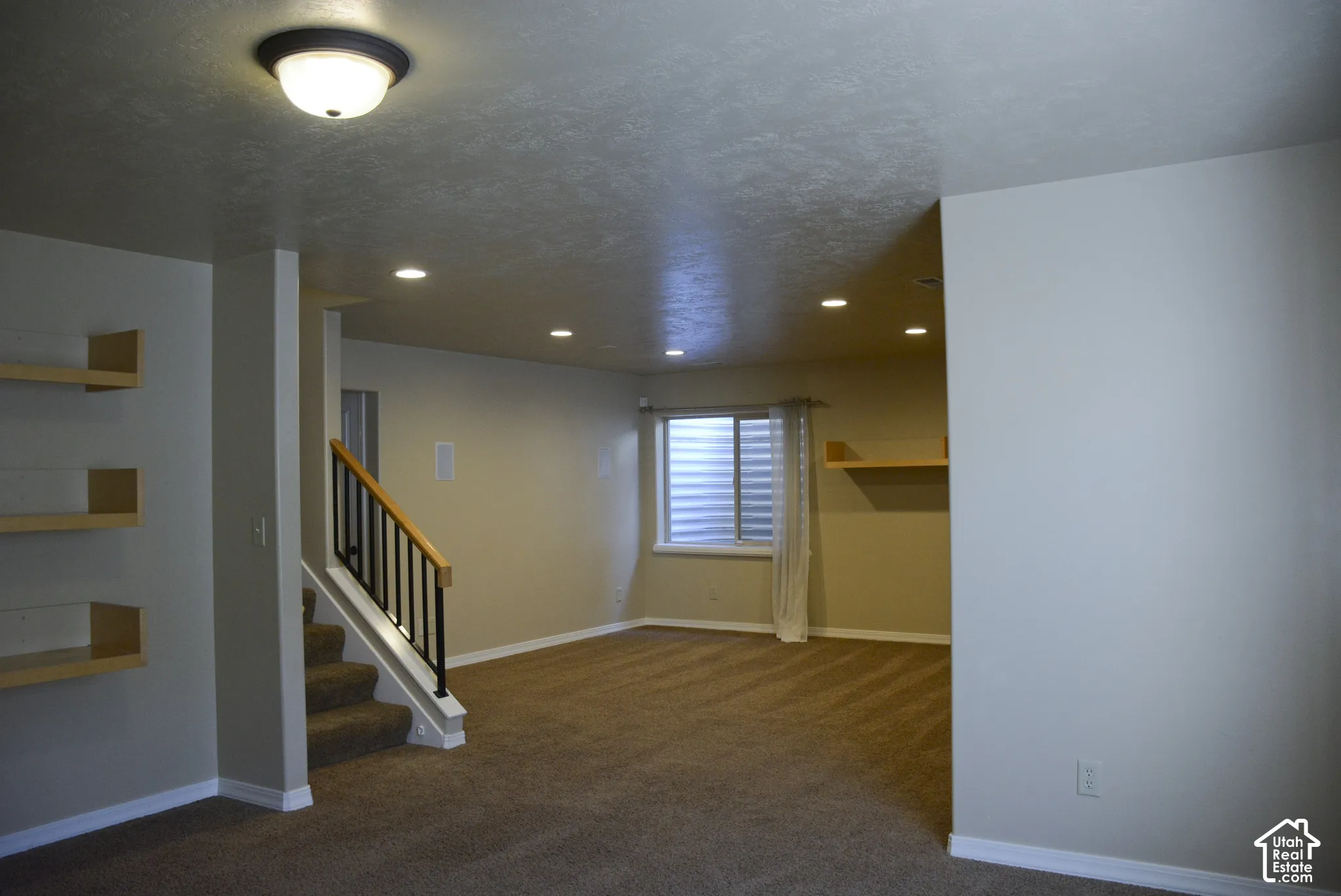 Carpeted flooring, recessed lighting, built-in shelving, staircase with wood handrail and black balusters, and a window with blinds