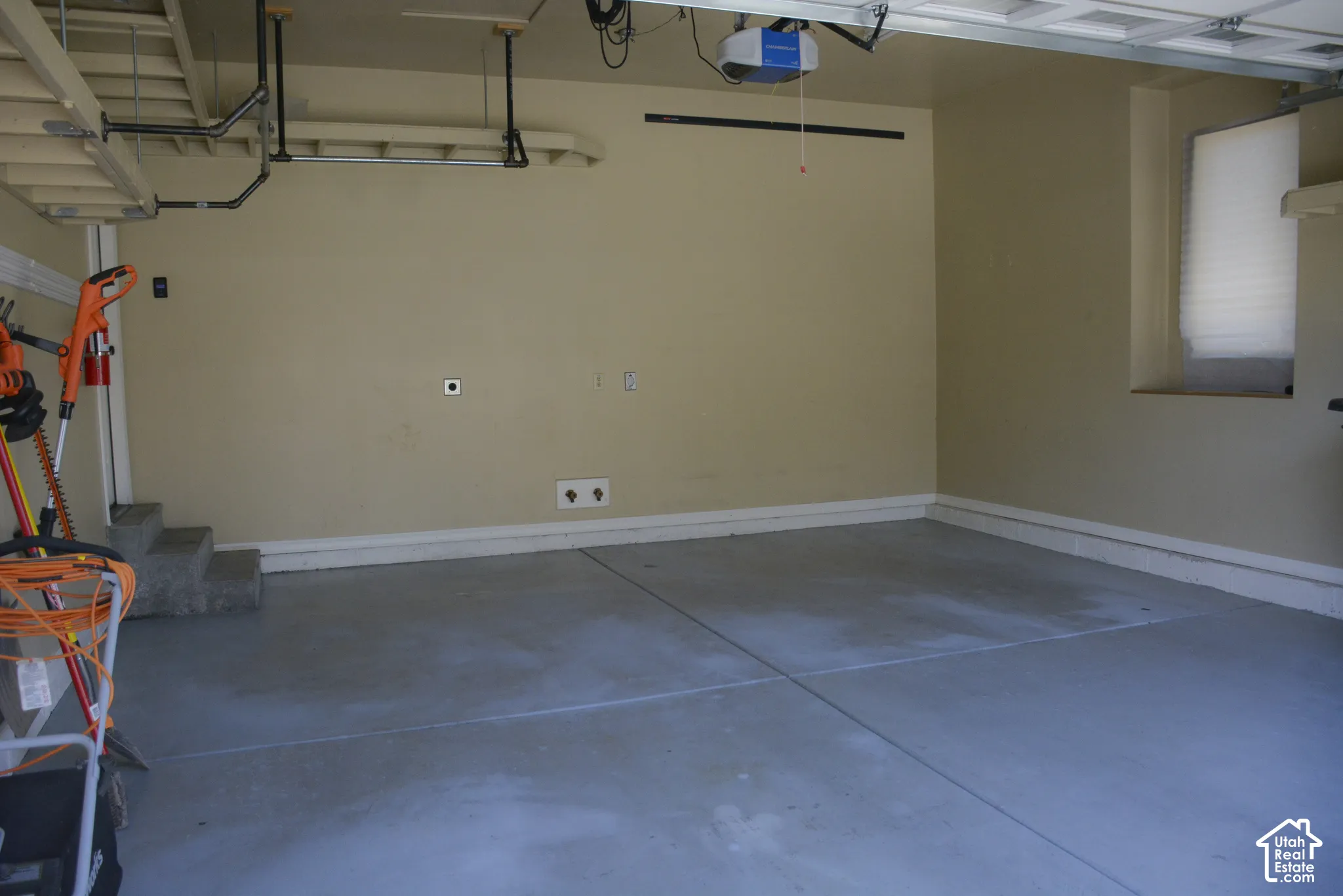 Concrete flooring, neutral wall paint, overhead garage door mechanism, steps, and a window with blinds