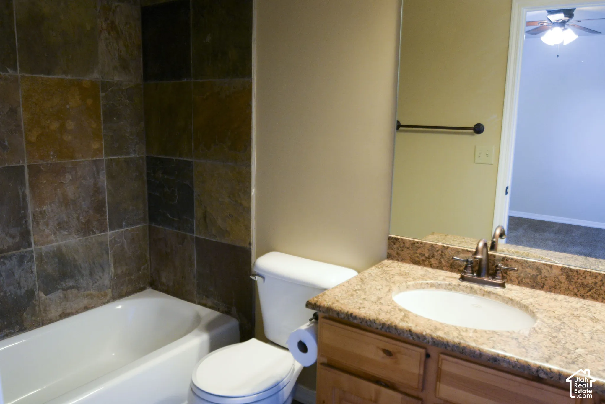 Bathtub with natural stone tile surround, toilet, vanity with integrated sink, and stone-finish countertop