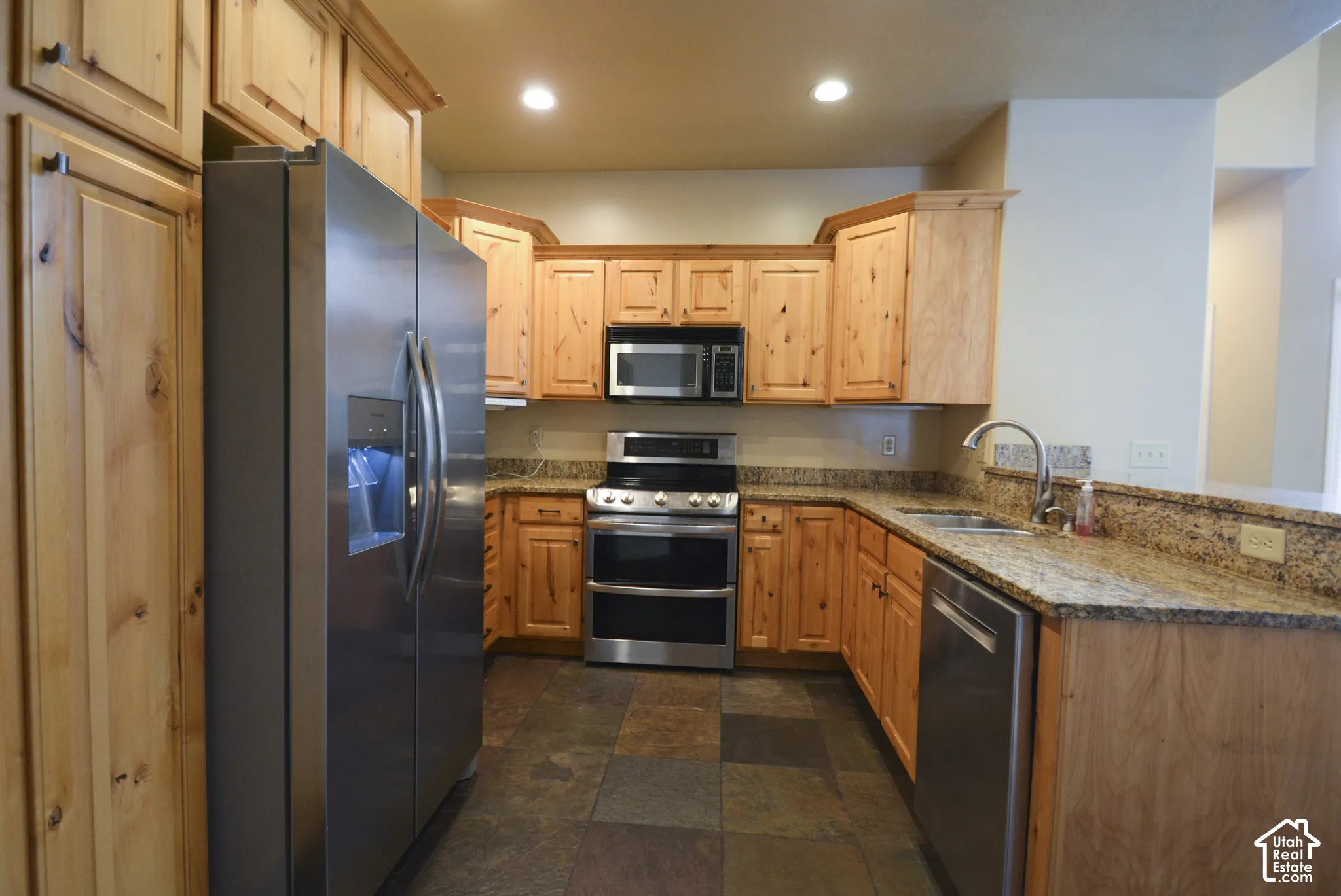 Kitchen featuring wood cabinetry, stainless steel appliances, granite countertops, and slate tile flooring