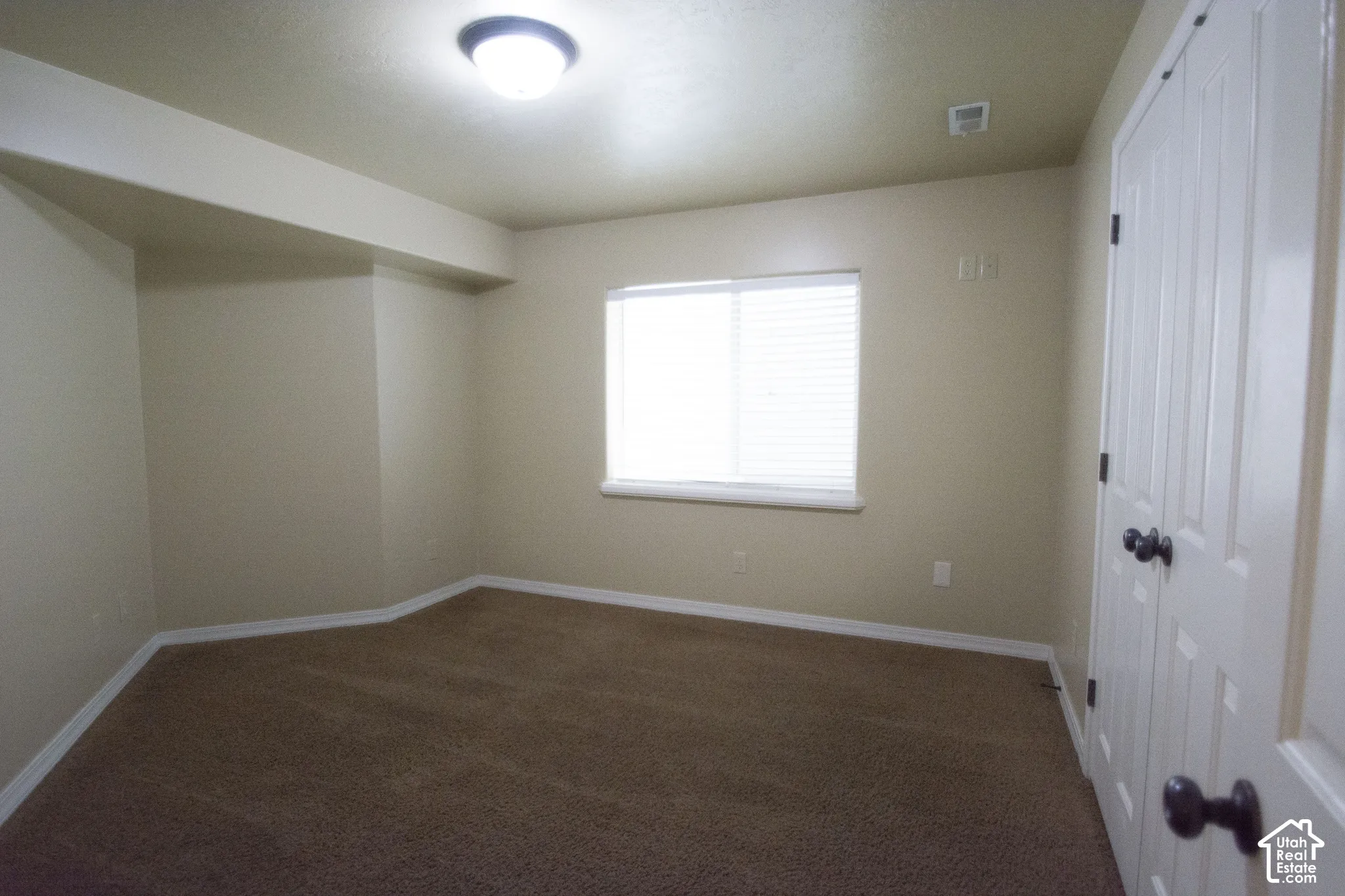 Wall-to-wall carpeting, window with blinds, ceiling-mounted light fixture, and white bi-fold closet doors with dark hardware
