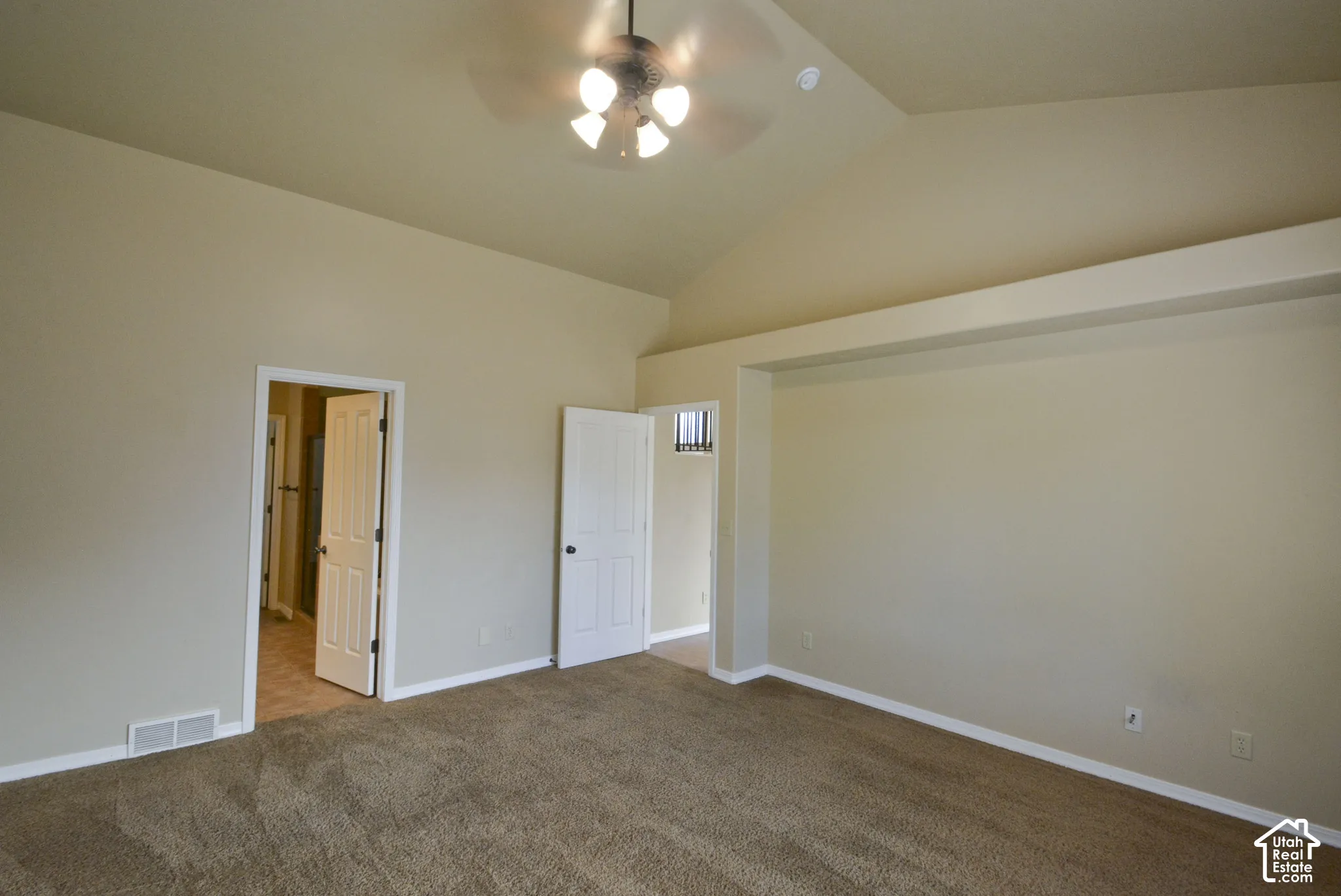 Vaulted ceiling with a ceiling fan, neutral wall paint, and carpeting