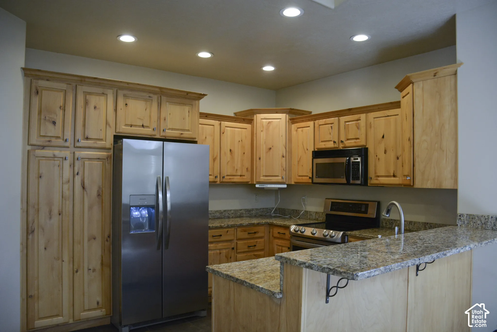 Kitchen featuring wood cabinetry, granite countertops, stainless steel refrigerator, stainless steel microwave, and a stainless steel range