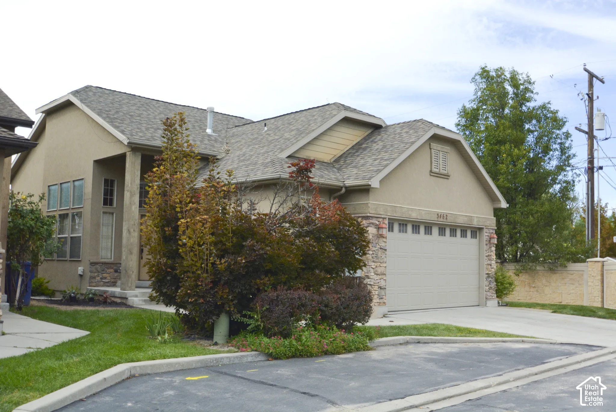 Stucco exterior with stone accents, attached garage, shingle roof, and mature landscaping