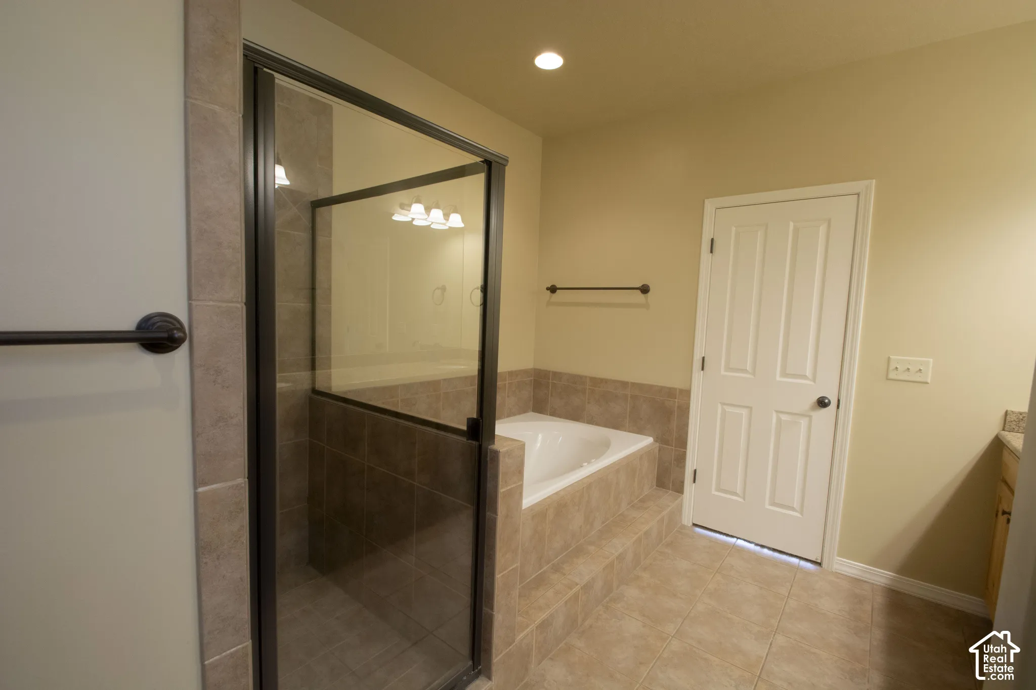 Tiled flooring complementing the shower and bath surround, featuring a glass-enclosed shower, a built-in soaking tub, and recessed lighting