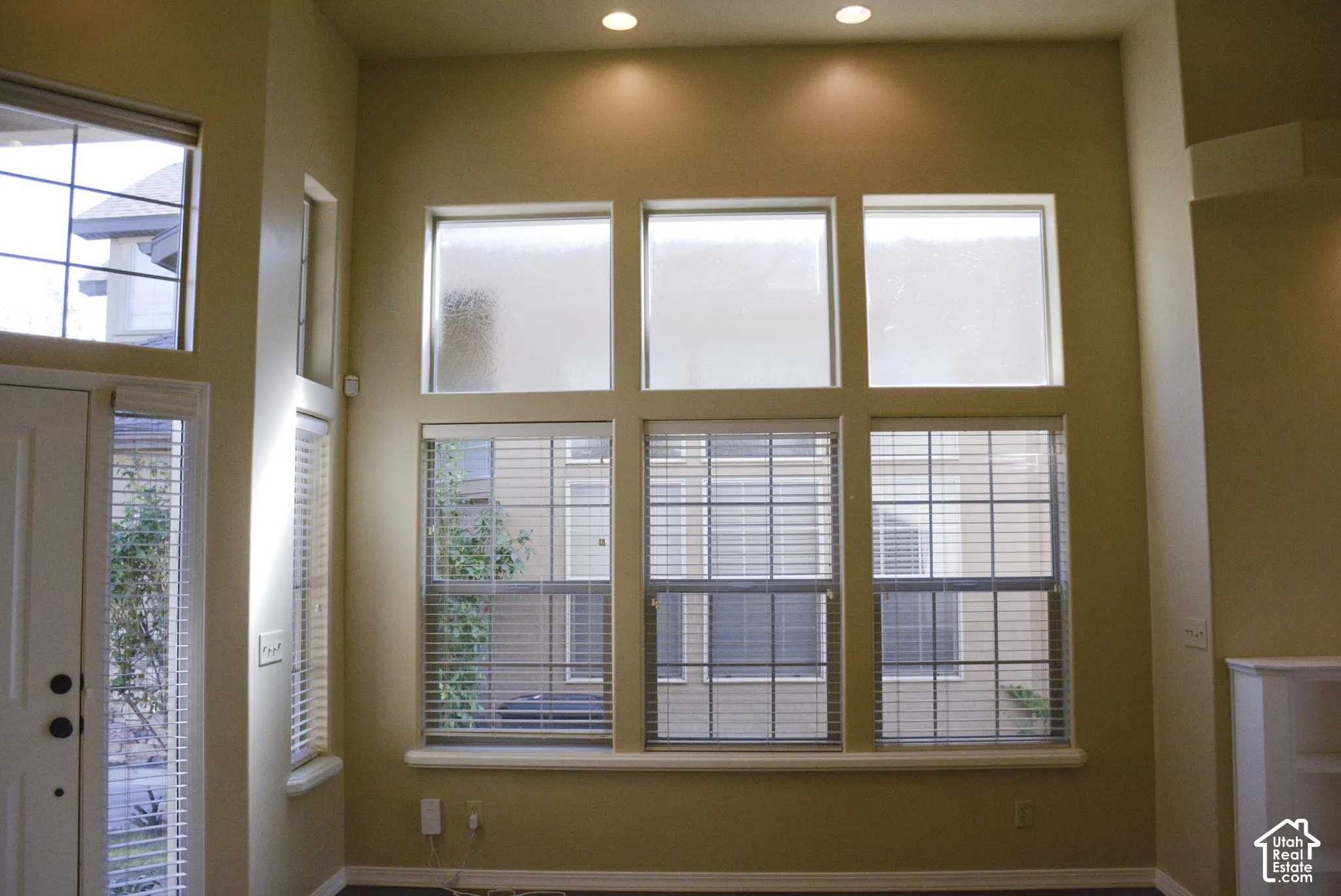 High ceilings with recessed lighting, multiple windows with blinds, wood-finish flooring, and a white paneled door with glass inserts