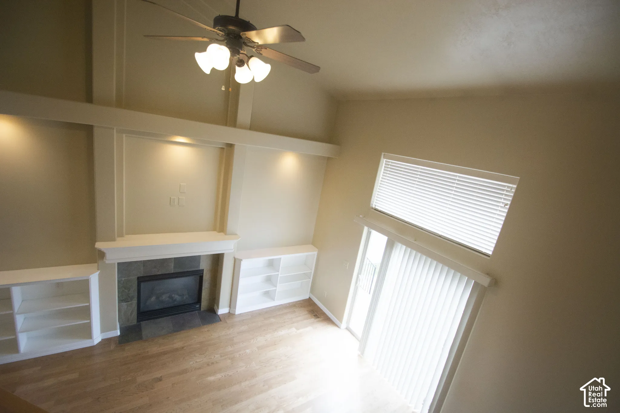 Vaulted ceiling with a ceiling fan, wood-finish flooring, built-in shelving, tile-surround fireplace, and a sliding glass door