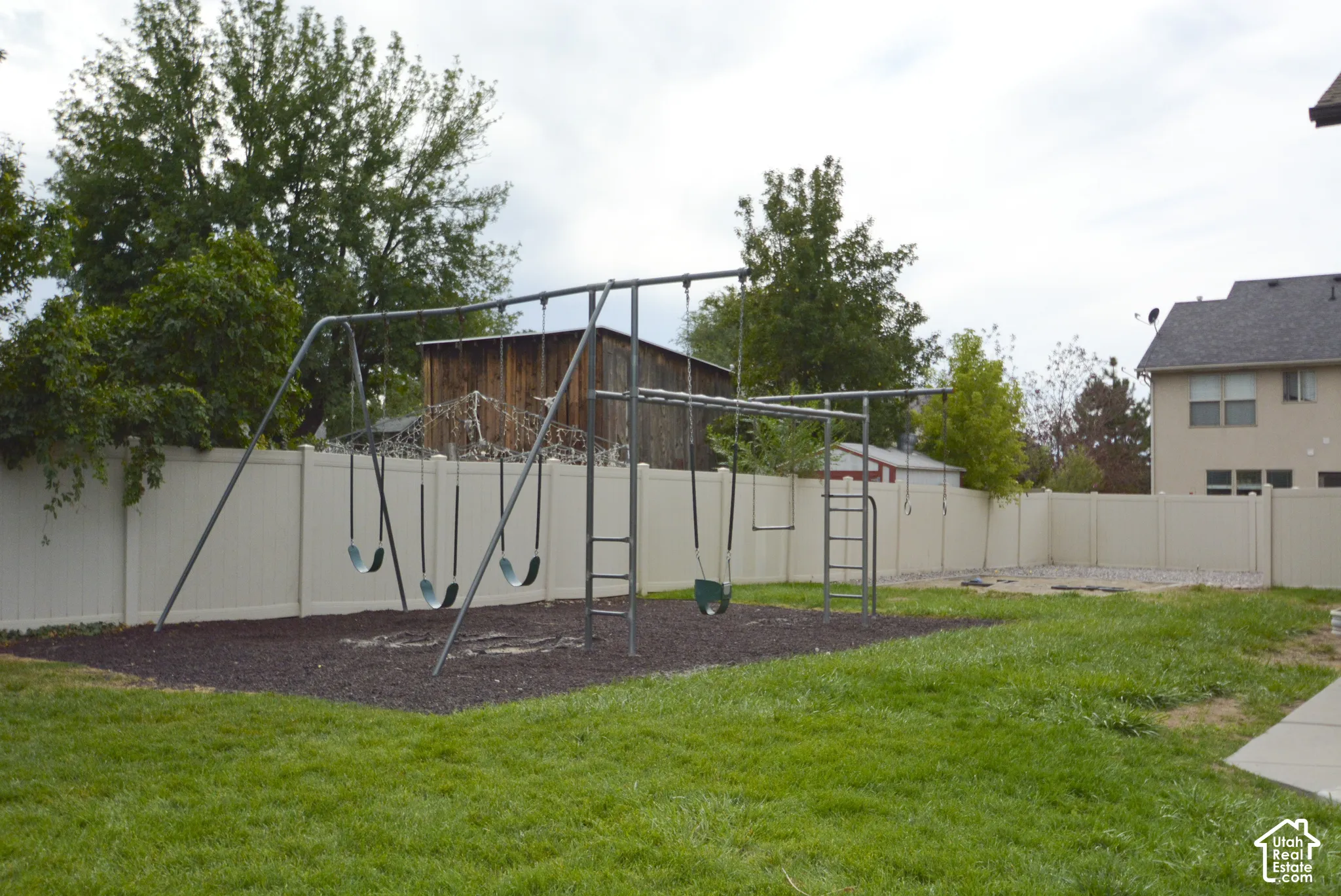 Expansive backyard featuring a manicured lawn, a swing set with a wood chip base, and a perimeter fence