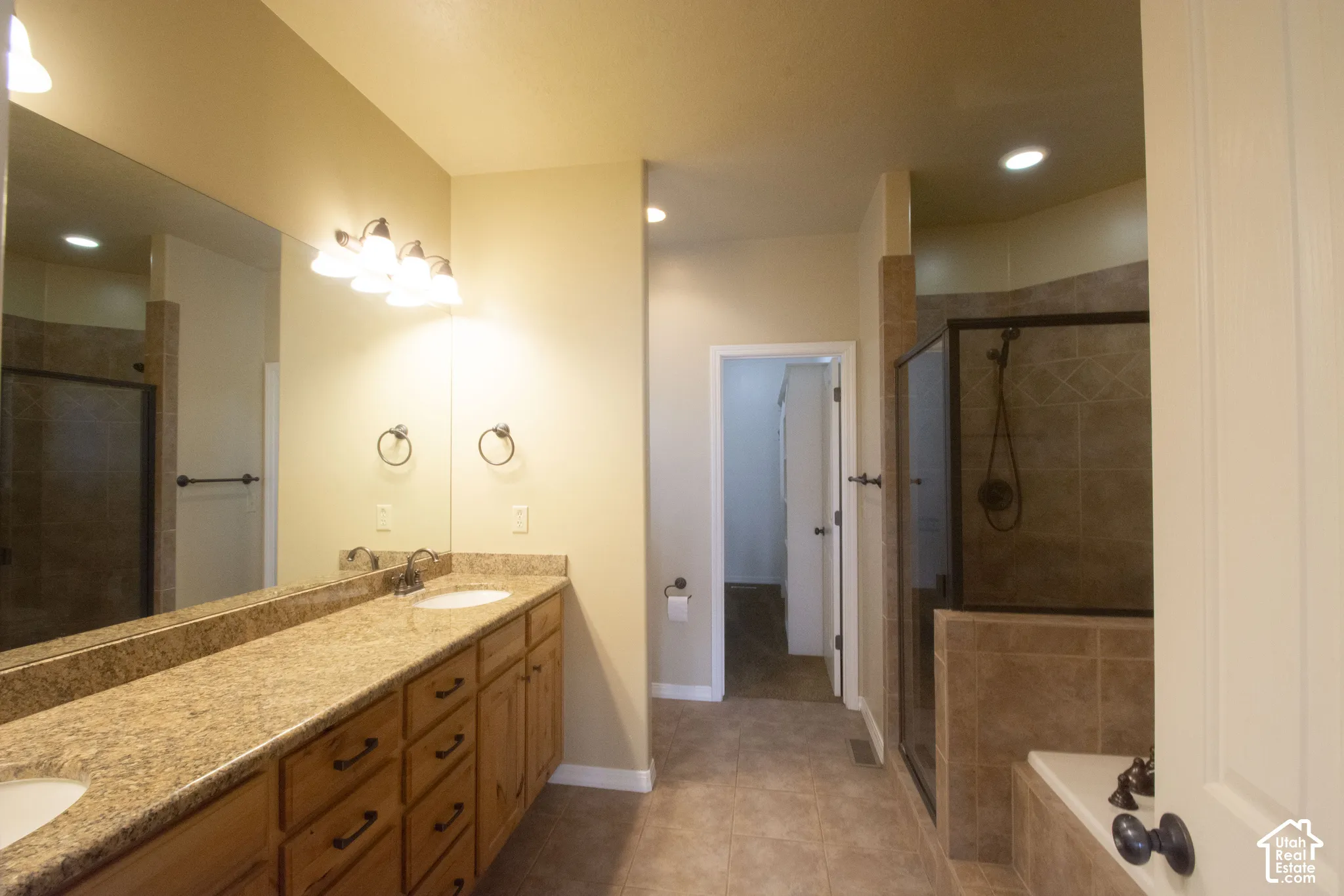 Dual vanity with integrated sinks, expansive mirror, wood-finish cabinetry, tile flooring, and a walk-in shower with a glass enclosure