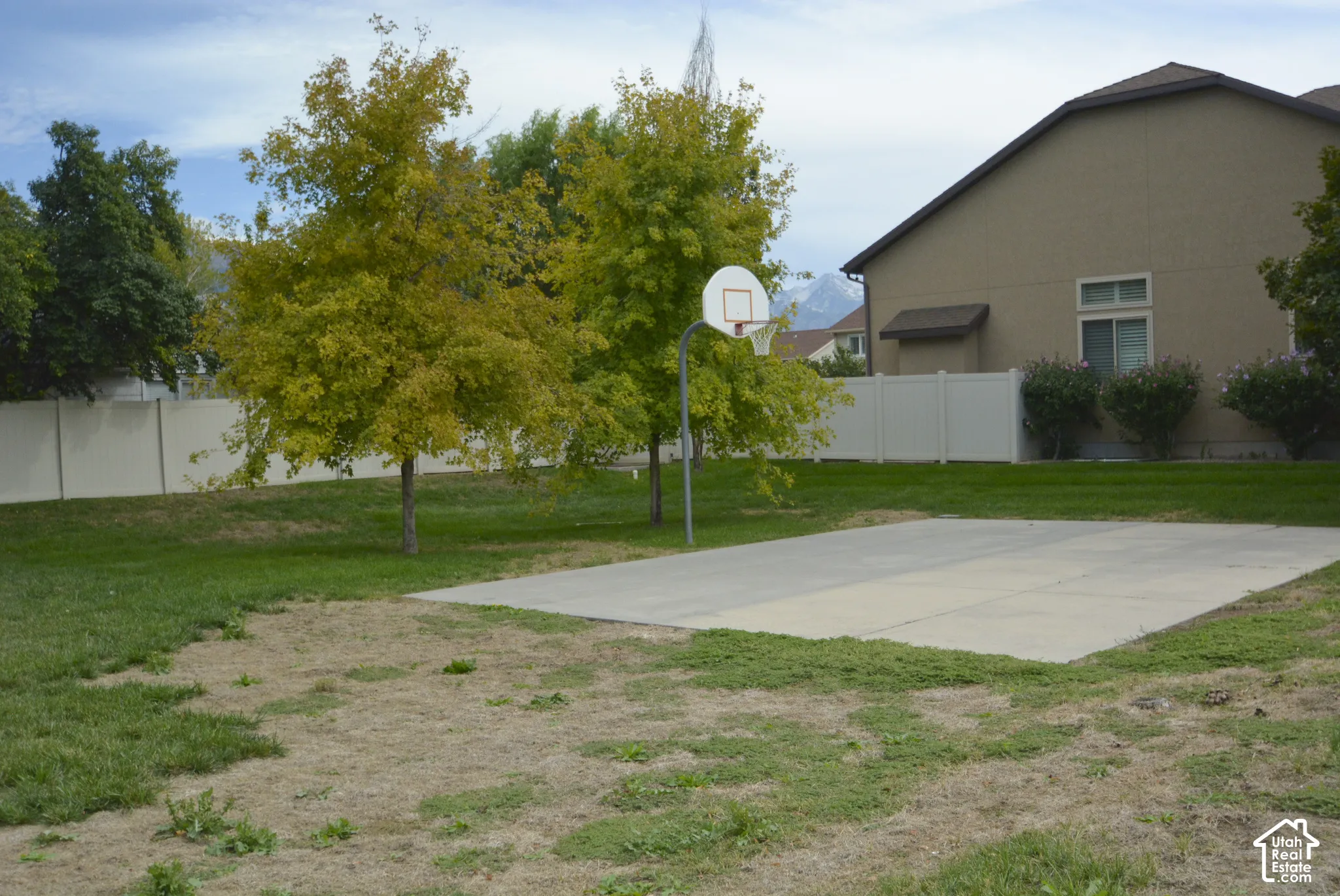 Basketball court with hoop, surrounded by a white privacy fence and mature trees