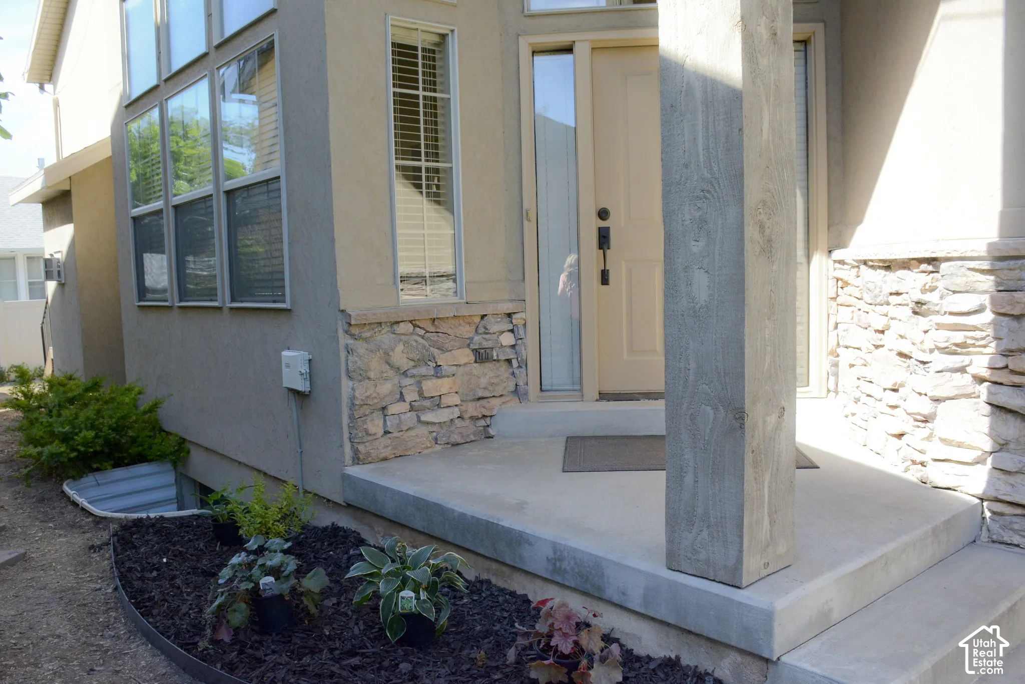 Concrete porch with wood-finish support columns, stucco exterior, and stone veneer accents