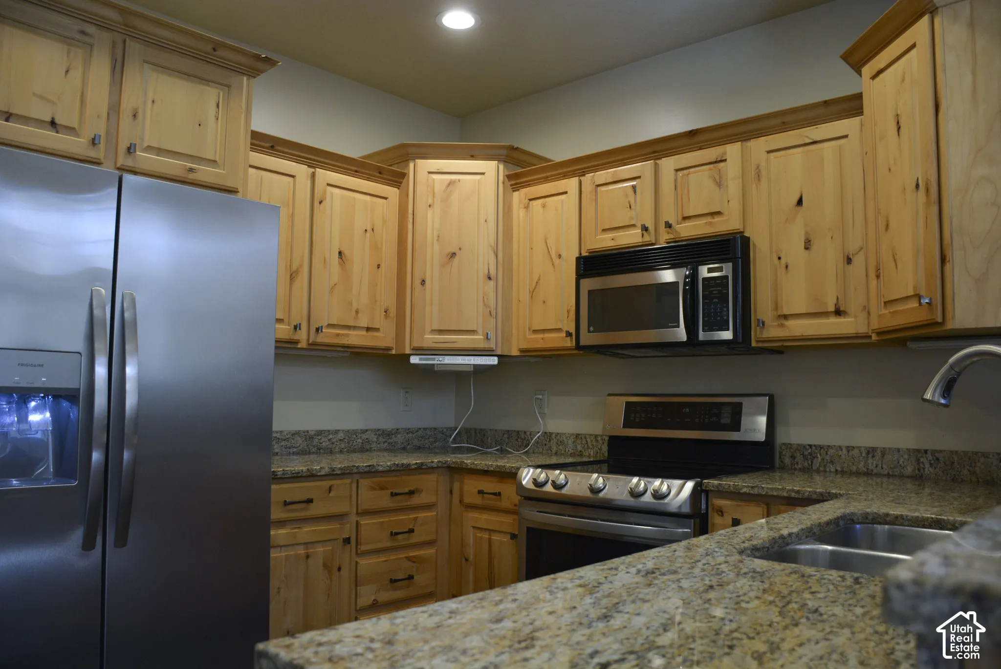 Kitchen featuring wood-finish cabinetry, stainless steel appliances, and stone countertops with an integrated sink