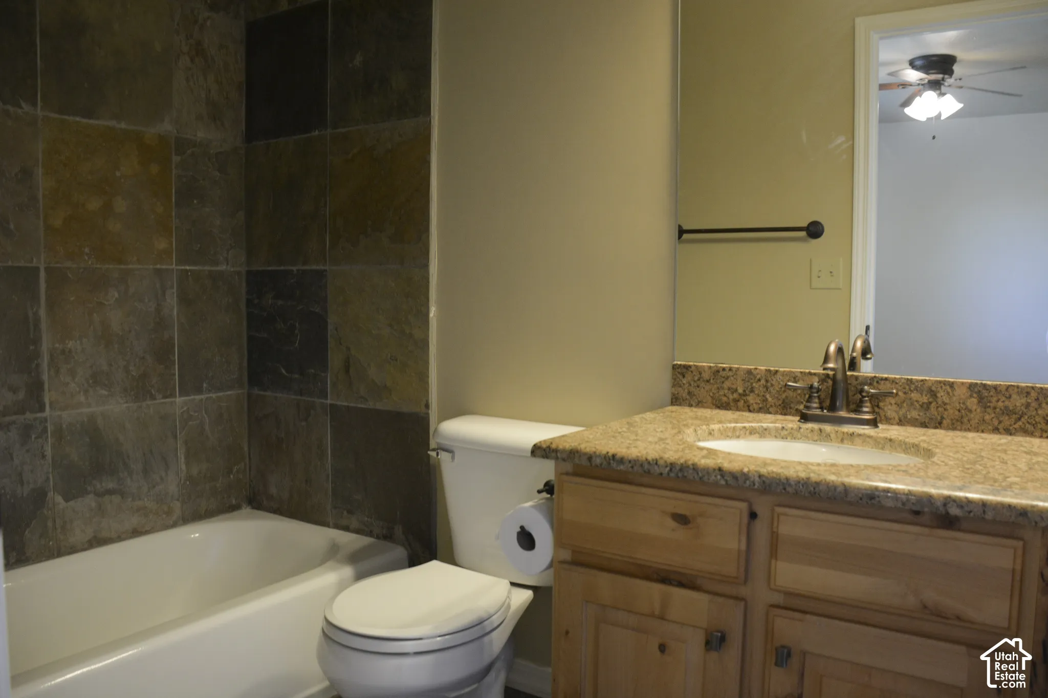 Tub-shower combination with square tile surround, wood-finish vanity with built-in sink, and stone-finish countertop