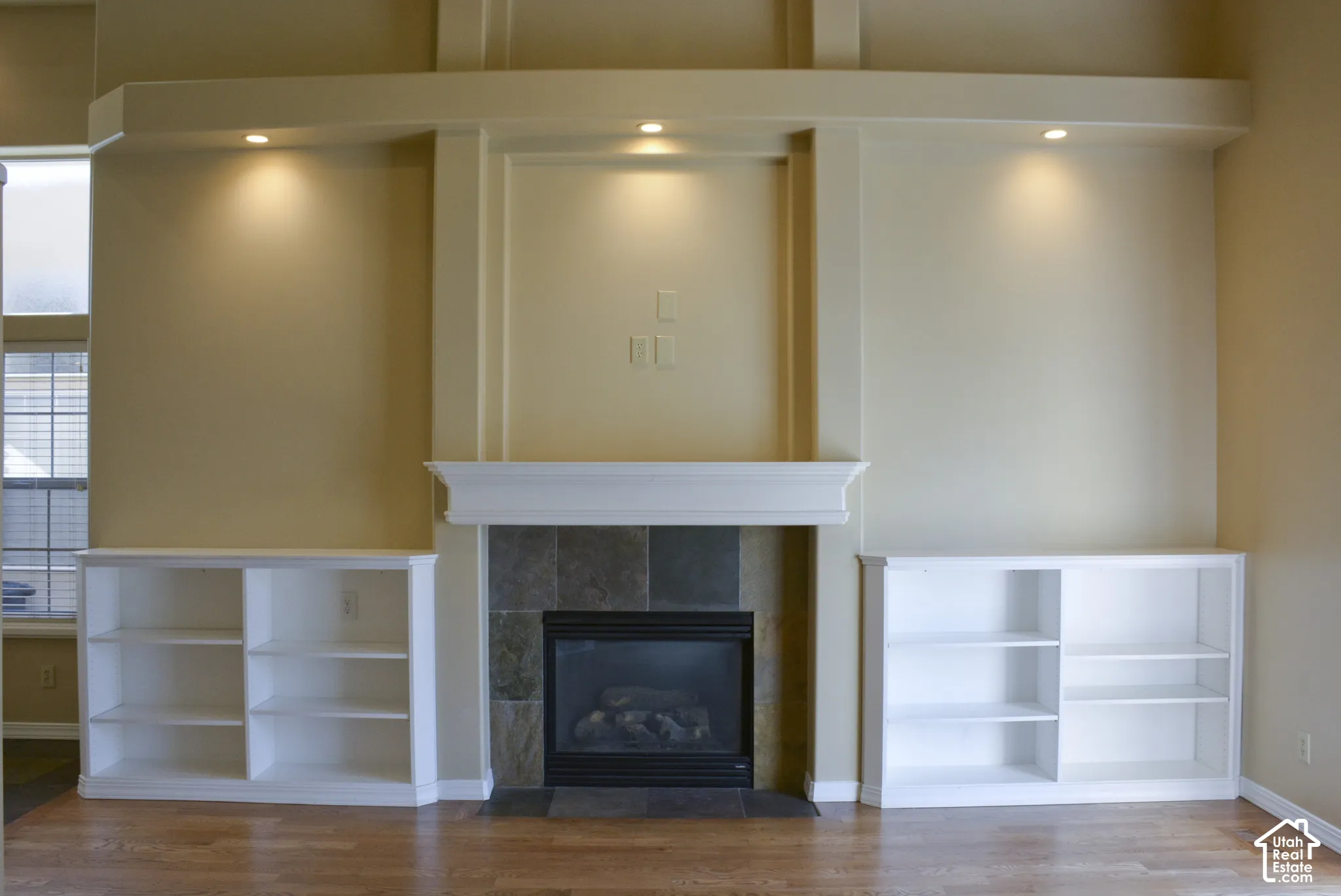 Hardwood-finish flooring, built-in shelving, stone tile fireplace surround, white mantel, and integrated recessed lighting