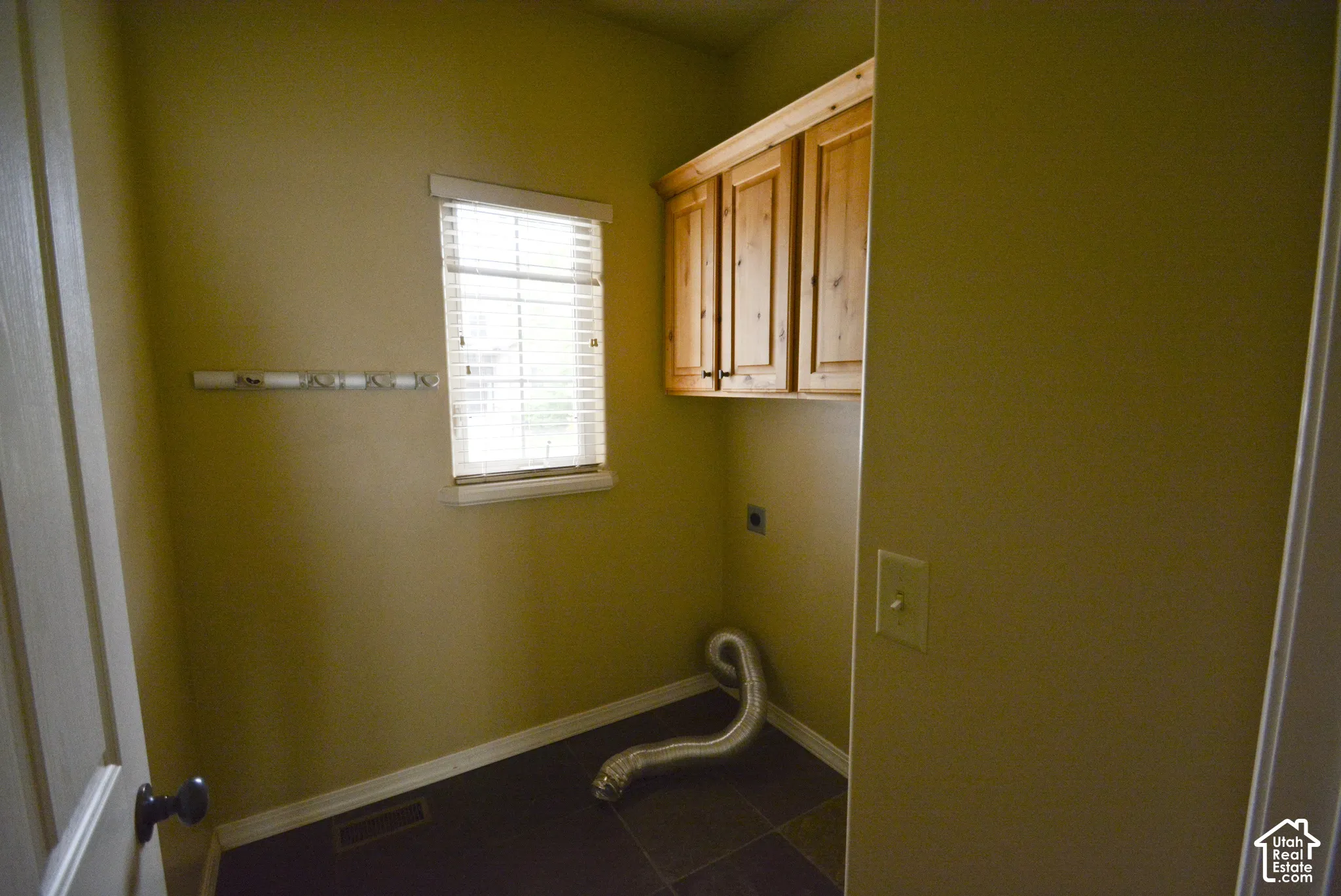 Window with horizontal blinds, wood-finish cabinetry, dark floor tile, and wall-mounted drying rack