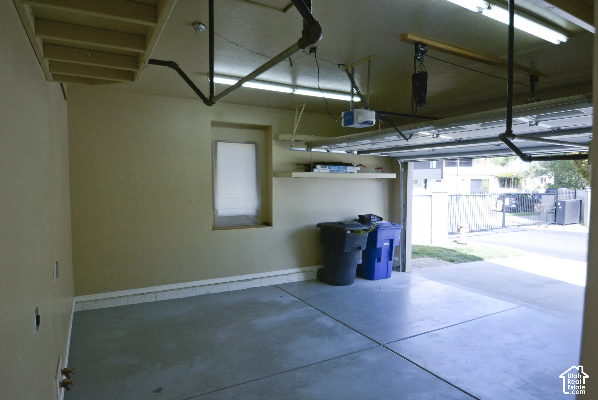 Spacious garage with concrete flooring, wall-mounted shelving, overhead lighting, and an automatic garage door opener